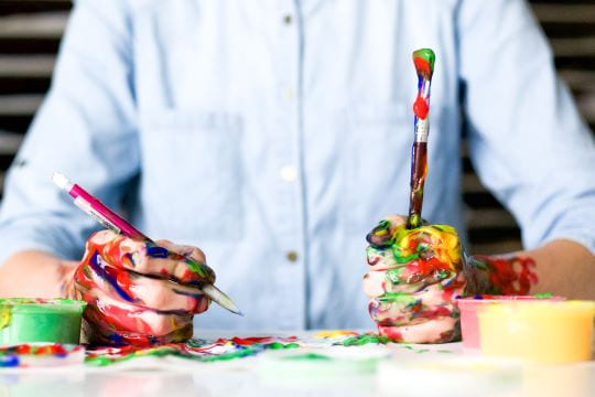 garçon qui tient deux pinceaux dans ses mains pleines de peintures pendant un babysitting à Paris 11