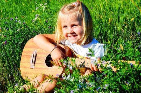 petite fille blonde qui sourit et joue de la guitare dans l'herbe lors d'un babysitting à Paris 11