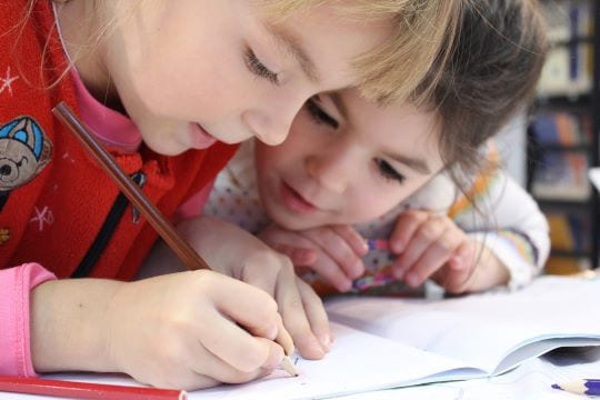 deux enfants proches qui écrivent dans un cahier lors d'un babysitting à Paris 17