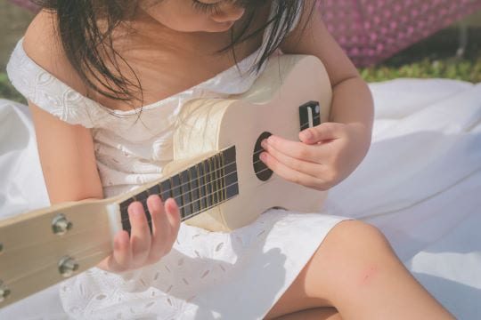 petite fille qui joue de la guitare dans l'herbe lors d'un babysitting à Paris 7